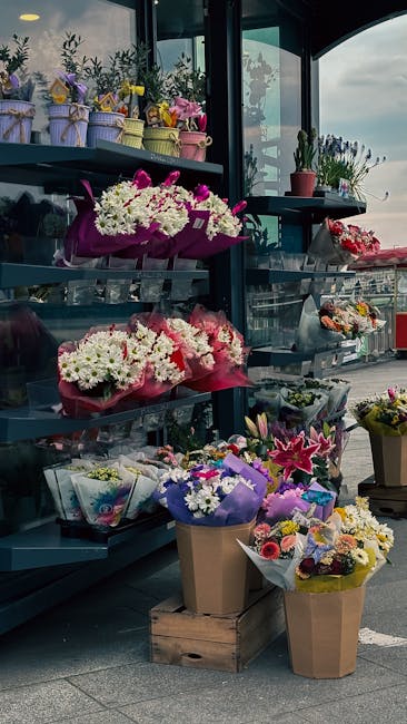 An outdoor display of various floral arrangements at a flower shop, featuring bouquets of fresh flowers including white chrysanthemums, pink carnations, purple lilies, and mixed seasonal blossoms wrap