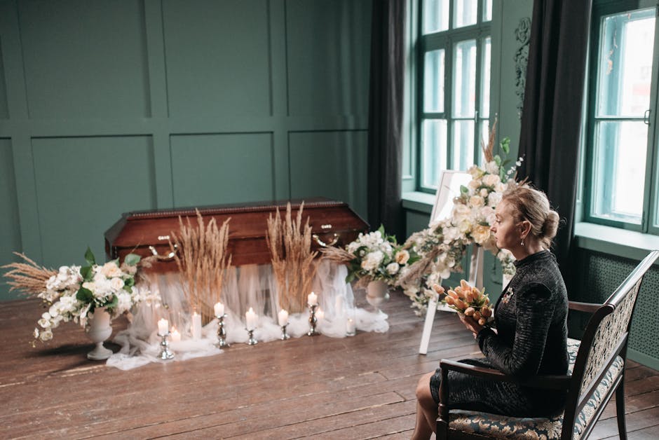 A woman seated in a vintage-style room with green-paneled walls and large windows, holding a bouquet of fresh, pastel-colored flowers. In front of her is a floral arrangement of white roses, peonies, 