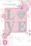 The image shows a beautifully crafted anniversary card that evokes the gentle intimacy of a long, shared life together in Norbury. The composition draws the eye first to the word LOVE, written in large, raised capital letters across the centre. Each letter is coated with soft, shimmering glitter, predominantly blush pink with hints of pearlescent white and silver, so that the word glows subtly, much like lamplight catching a crystal vase on a Norbury mantelpiece. The O is shaped with a graceful curve, echoing the outline of a tender heart without overtly becoming one. Around this central word, an airy wreath of illustrated blossoms and looping vines seems to drift across the card. The flowers, painted in hushed tones of pastel pink, mauve, and pale grey, have a washed, almost watercolor quality, as if lightly brushed onto the page by hand. Fine lines and tiny silver accents pick out petals and leaves, giving just enough detail to suggest the care and artistry of a local florist designing a romantic arrangement for same-day delivery nearby. The background is a soft, even blush pink, neither too bright nor too pale, providing a calm field for the floral pattern to float upon. Delicate, scripted phrases such as On Our Anniversary and I love you today and always are tucked gracefully among the blooms, written in a flowing font that feels personal and sincere, like a handwritten note composed at a café off London Road. Overall, the card conveys a whisper-soft sense of celebration, tender and enduring, perfectly matched to a quiet evening at home with flowers close by.
